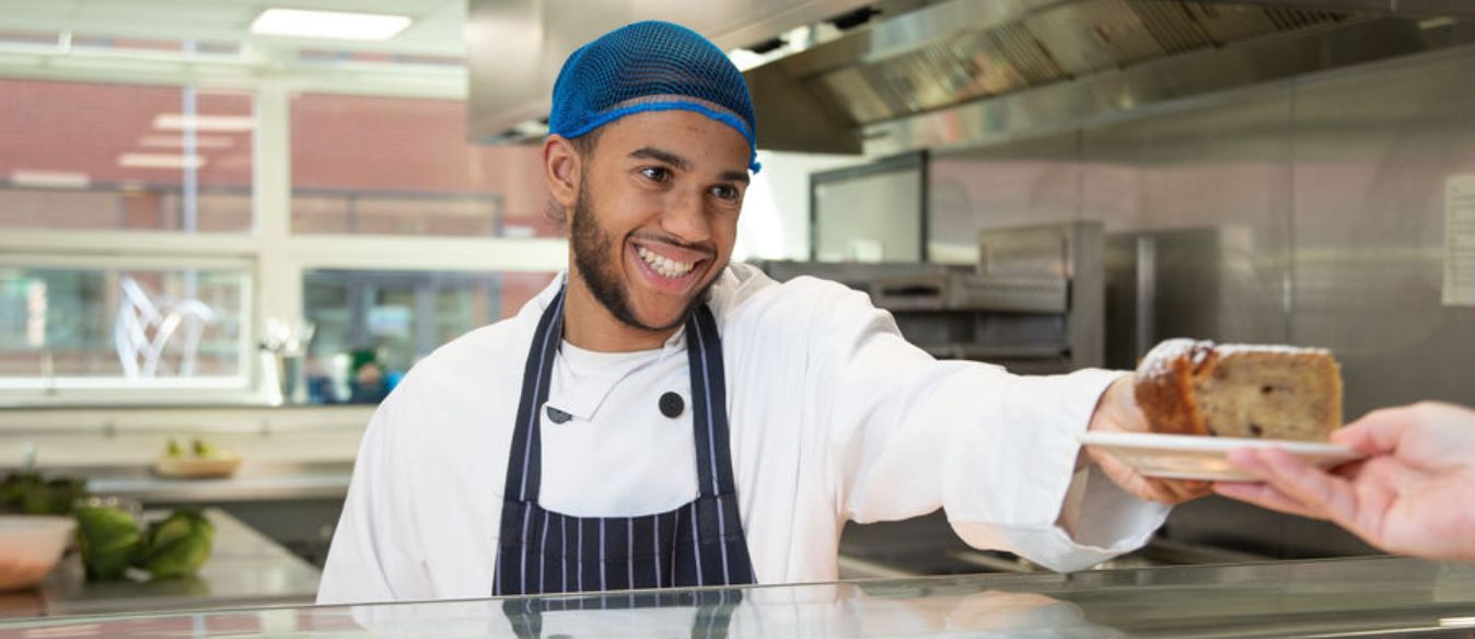 A smiling inclusive learning student proudly holds a slice of cake, showcasing their culinary creation with joy and enthusiasm.